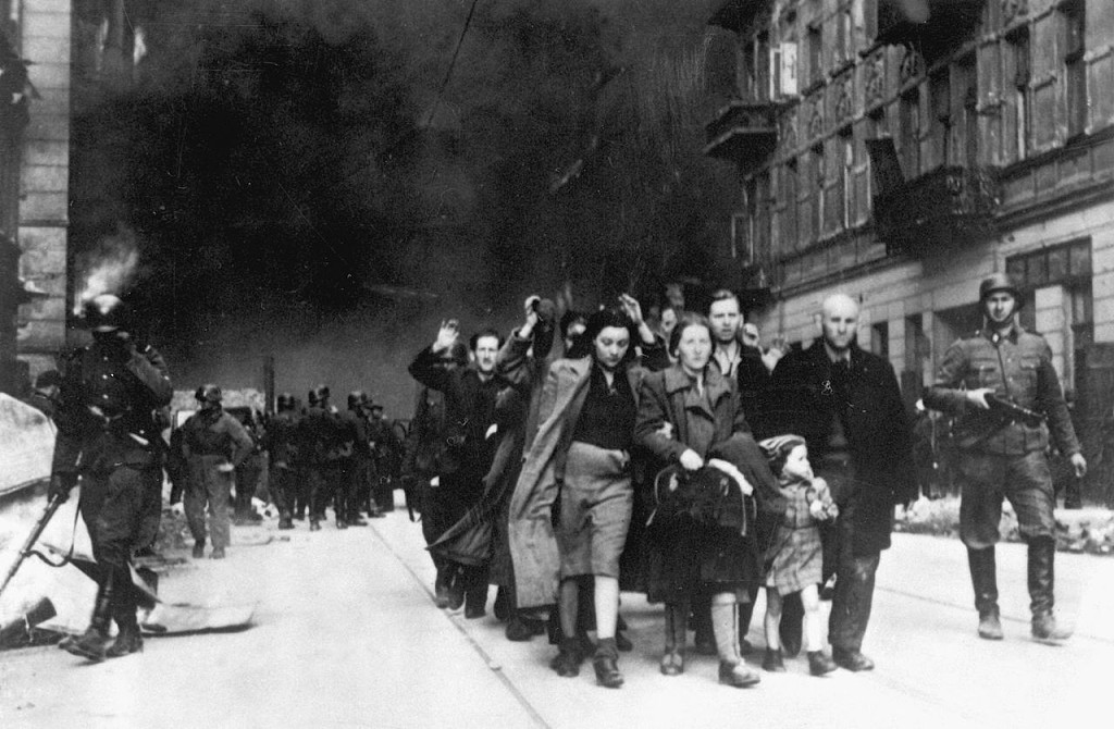 Stroop Report original caption Forcibly pulled out of dug-outs. Captured Jews are led by German troops to the assembly point for deportation. Picture taken at Nowolipie street, near the intersection with Smocza.jpg